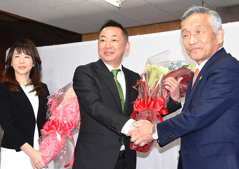 鳥取・日吉津村長選で無投票の初当選が決まり、現職の石操村長(左)と握手を交わす中田達彦氏(中央)ら=同村日吉津で、阿部絢美撮影