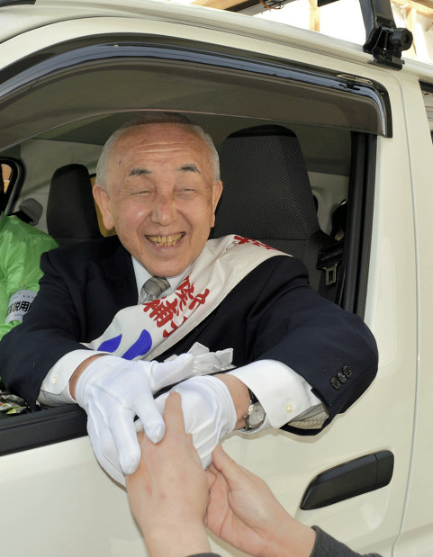 車に駆け寄る支持者に満面の笑みで応え握手する小池清彦氏=新潟県加茂市で