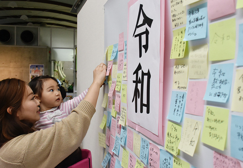 新元号「令和」への思いを書いた紙を貼り付ける親子=鳥取市国府町町屋の因幡万葉歴史館で、園部仁史撮影