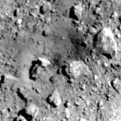 人工クレーターを作った後の表面。中央付近にくぼみができて暗くなっている=JAXA、東京大など提供
