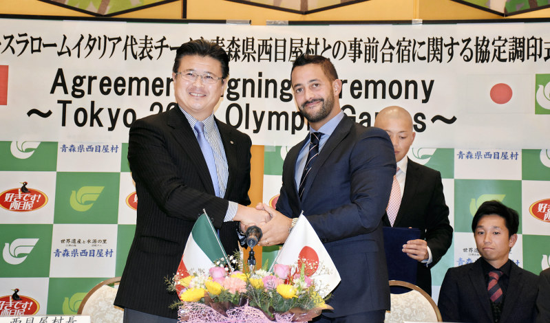 事前合宿に関する協定書にサインし、握手する西目屋村の関和典村長(左)とダニエレ・モルメンティさん=青森県西目屋村で