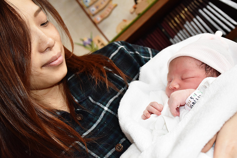 生まれたばかりの長女凛ちゃんを抱く村上朋恵さん。腕に巻いた標識には「5月1日」の記述も=鳥取市叶のみやもと産婦人科医院で、小坂春乃撮影