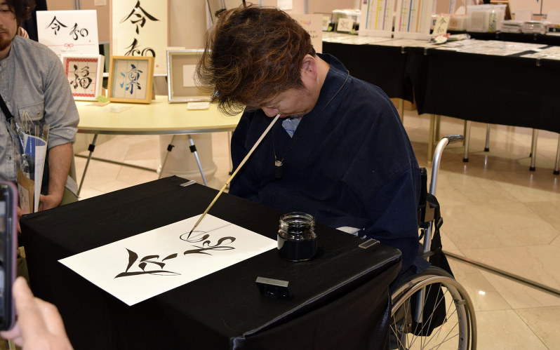 口を使い巧みに筆を操って「令和」と描く浦上秀樹さん=横浜市中区で