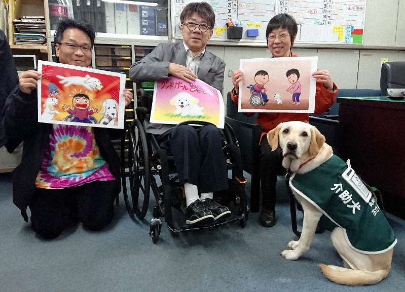 制作中の紙芝居「グッドガール シンシア」を持つ風太郎さん(左端)と木村佳友さん、美智子さん夫妻と介助犬デイジー=兵庫県尼崎市のピッコロ劇団事務所で、2019年4月28日午後2時44分、高尾具成撮影