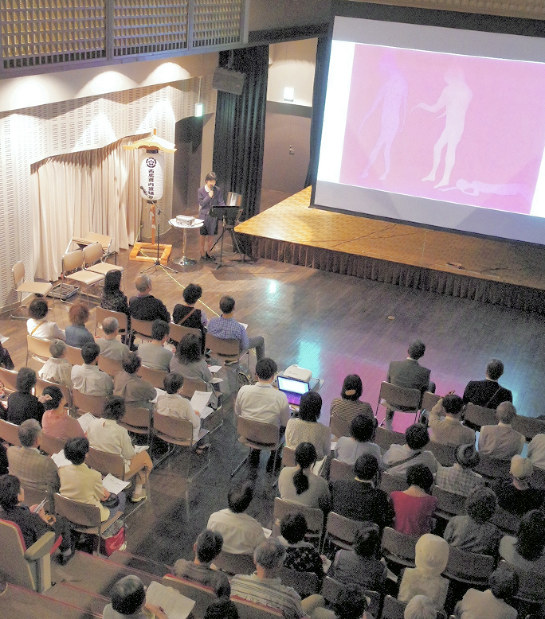 スクリーンに映し出された「紙芝居」を見ながら朗読を聞く人たち=秋田県羽後町で