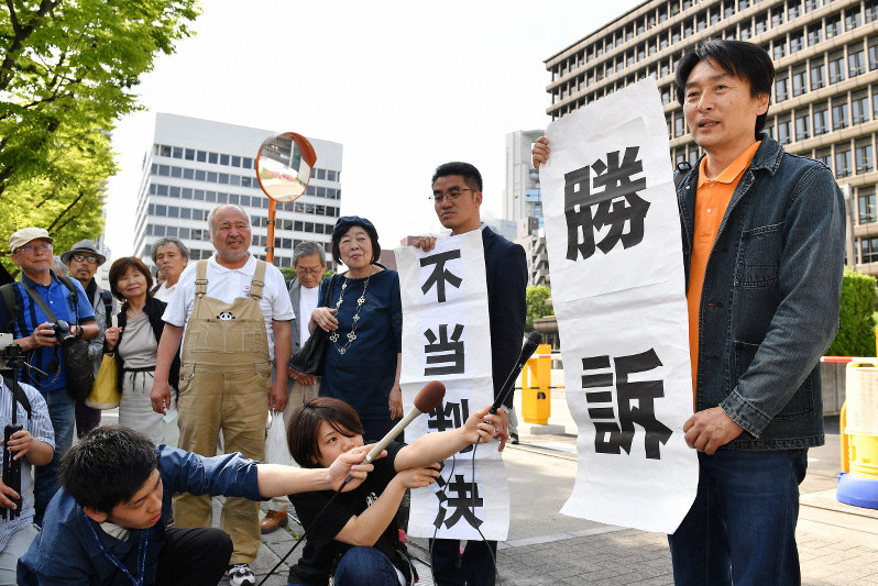 判決後に大阪地裁前で「勝訴」と書かれた幕を掲げる原告の木村真・大阪府豊中市議(右)=大阪市北区で2019年5月30日午後3時11分、木葉健二撮影