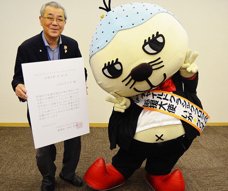 応援大使のたすきを掛けたいが☆グリオと任命状を持った三重・伊賀市文化都市協会の中村忠明理事長=同市の市文化会館で、大西康裕撮影