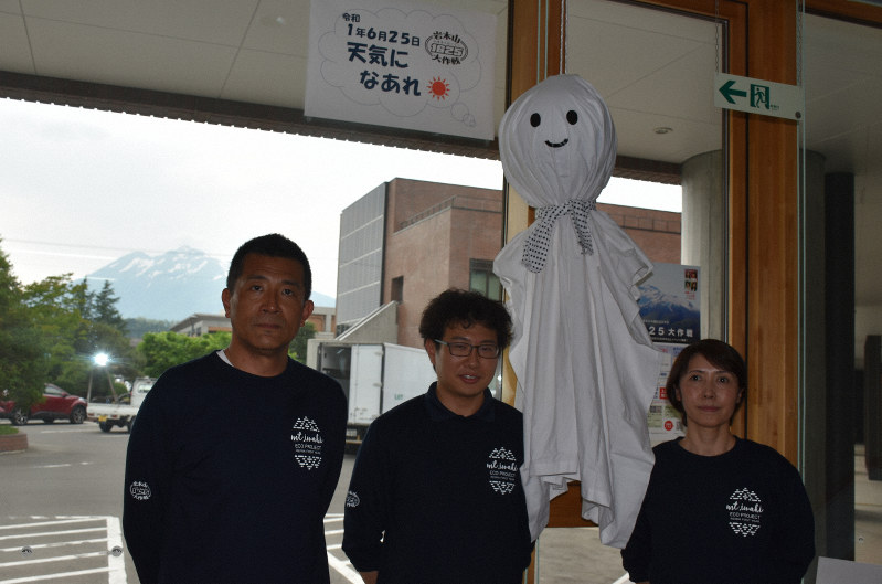 イベント当日の快晴を祈り、巨大てるてる坊主をつり下げた岩木地区地域おこし協力隊の3人=弘前市岩木庁舎で2019年6月5日、藤田晴雄撮影