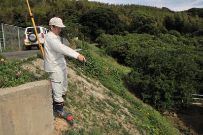 大雨に削られる被害を受けた土手を指さす朝倉さん