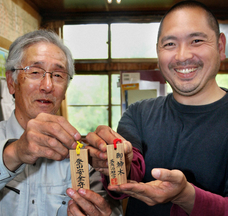 倒れた杉の木で作った、サポーター特典の限定「登山安全守」を手にする高千穂秀敏・英彦山神宮宮司(左)と長男の有昭祢宜=福岡県添田町の英彦山神宮で2019年5月13日午後4時6分、山本泰久撮影