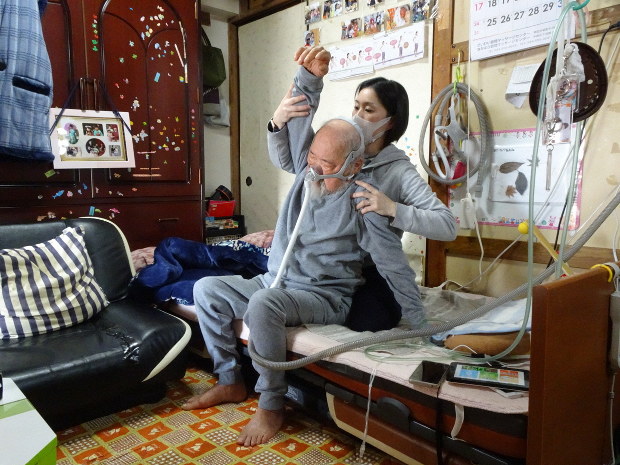 石山さん(奧)によるリハビリを受ける田島さん。リハビリの際は人工呼吸器を装着する=川崎市内で2019年3月20日、鈴木敬子撮影