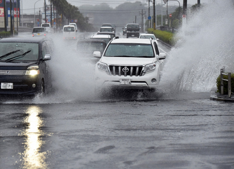 冠水した道路を水しぶきをあげて走行する乗用車=鹿児島市で2019年7月3日午後4時58分、森園道子撮影(画像の一部を加工しています)