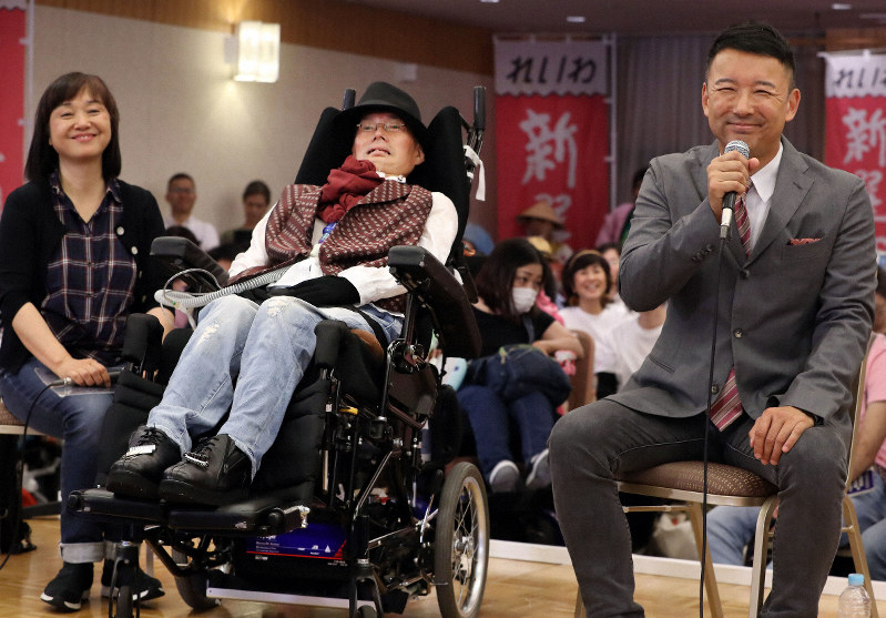 当選確実となった舩後靖彦氏(中央)とインタビューを受け、笑顔を見せるれいわ新選組の山本太郎代表(右)。左は介助者の佐塚みさ子氏=東京都千代田区で2019年7月21日午後9時58分、小川昌宏撮影
