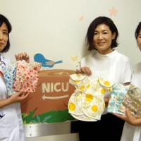 「ススリレ」の新作の肌着を手にする（左から）京都府立医大病院看護師の中島輝美さん、製作者の奥村由乃さん、亡くなった長女に肌着を着せていた小川あゆみさん＝京都市上京区で2019年7月23日、国本ようこ撮影