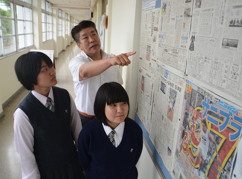 廊下に貼られた新聞に目を通す峯近卓美校長(中央)と生徒ら=泉鳥取高で