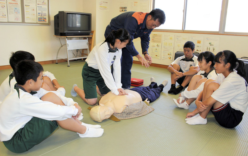 人形を使い、消防職員(中央)から心臓マッサージを学ぶ中学生たち=伊東消防署救急指導室で