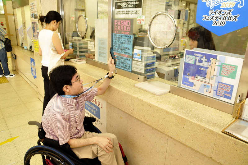 西武・高田馬場駅の窓口で、スマホの「ミライロID」登録情報画面を提示する磯谷さん=西武鉄道高田馬場駅で