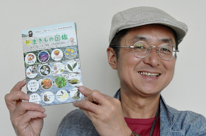植物から動物まで1冊にまとめ、持ち運びにも便利な「新・生きもの図鑑」をPRするNPO法人「地球と自然」の中西崇雄理事長=三重県名張市役所で、衛藤達生撮影