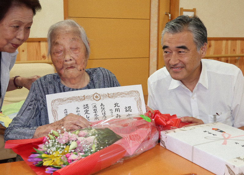 滋賀県内最高齢の北川みなさん(中央)に花束などを渡す滋賀県彦根市の大久保貴市長(右)。左は長女喜美さん=同市城町2の特別養護老人ホーム「さざなみ苑」で、西村浩一撮影