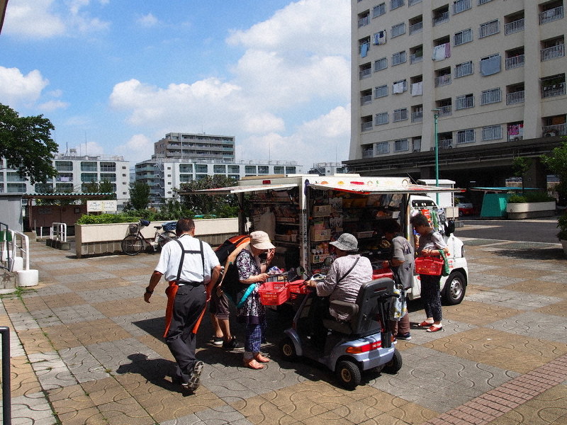 板橋区西台のアパートの玄関口に停車したとくし丸で買い物をする住民たち