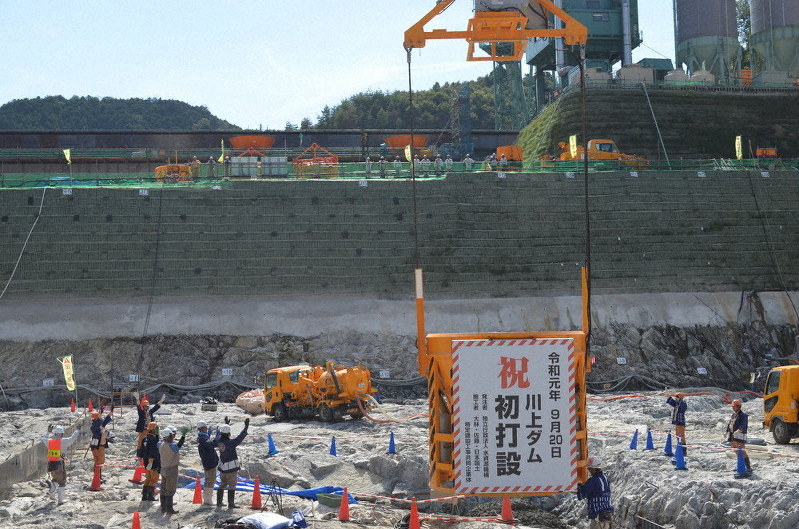 初打設を祝う看板を付けクレーンにつるされ、コンクリートを流し込んだバケットと万歳する工事関係者=三重県伊賀市で、大西康裕撮影