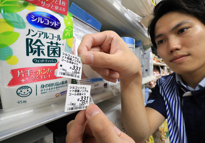 増税に伴い差し替えた消費税10%の新しい値札(上)と古い値札を見せるコンビニエンスストアの従業員=東京都品川区のローソン大井店で2019年10月1日午前0時、梅村直承撮影