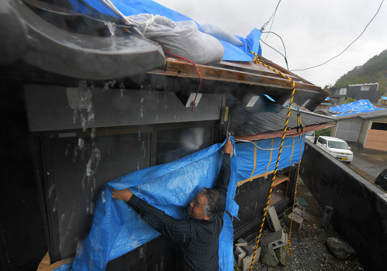 台風19号の接近に備え、風雨が強まる中、ガラス窓にビニールシートを張る庄司一則さん=千葉県館山市布良で2019年10月11日午後0時48分、手塚耕一郎撮影
