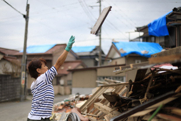 台風15号の強風で吹き飛ばされたがれきを片付ける女性。多くの住宅の屋根はブルーシートに覆われていた=千葉県鋸南町大帷子で2019年9月13日