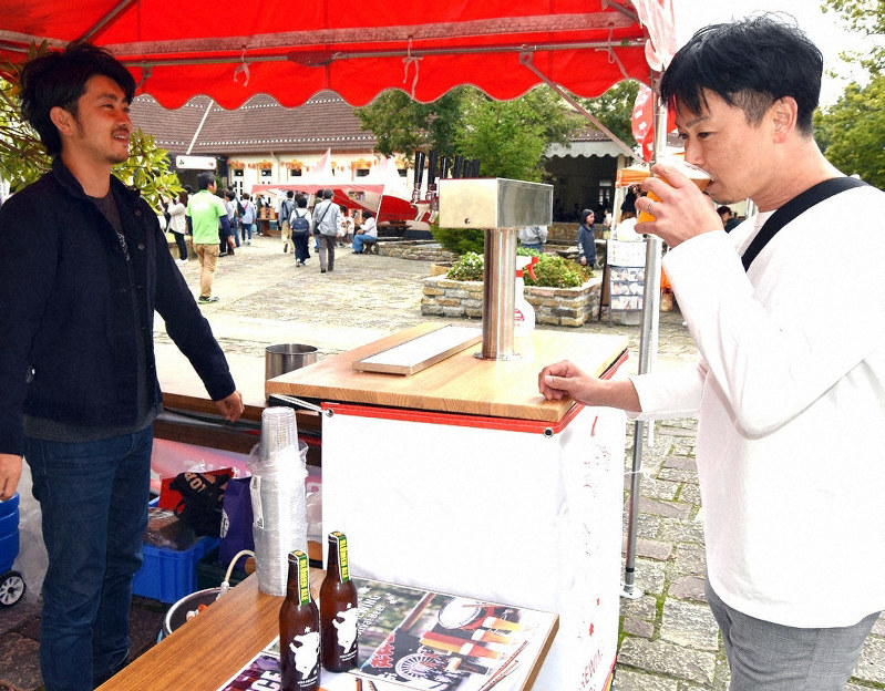 「ヒノブルーイング」の田中宏明社長(左)から説明を受けながら、クラフトビールを味わう来園者=日野町西大路の滋賀農業公園ブルーメの丘で、蓮見新也撮影
