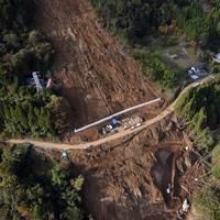 台風19号による土砂崩れで大きくえぐられた山肌。中央の道路沿いに行方不明となっている佐々木睦さん、定子さん夫婦の自宅跡があり、その下では2人の捜索が続く=相模原市緑区牧野で2019年11月8日、本社ヘリから北山夏帆撮影