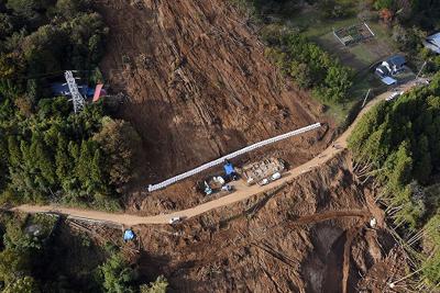 台風１９号による土砂崩れで大きくえぐられた山肌。中央の道路沿いに行方不明となっている佐々木睦さん、定子さん夫婦の自宅跡があり、その下では２人の捜索が続く＝相模原市緑区牧野で２０１９年１１月８日、本社ヘリから北山夏帆撮影