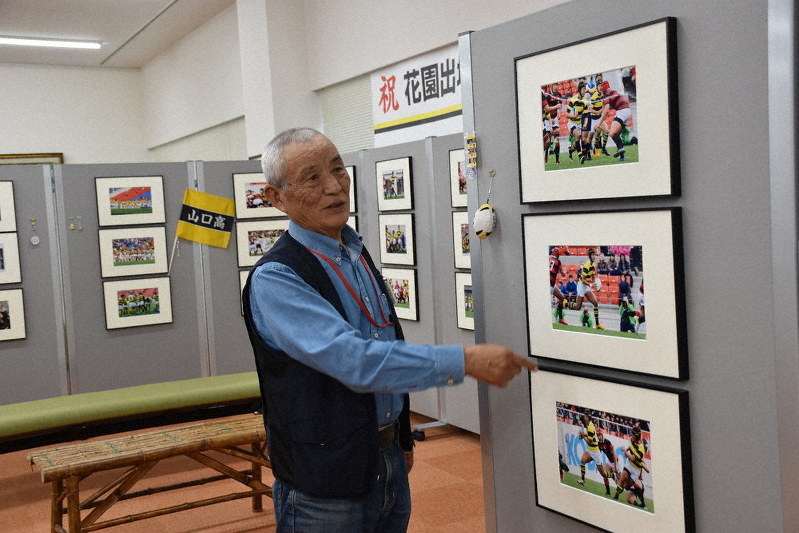 花園で健闘した山口高ラグビー部の写真が並ぶ会場と松岡さん