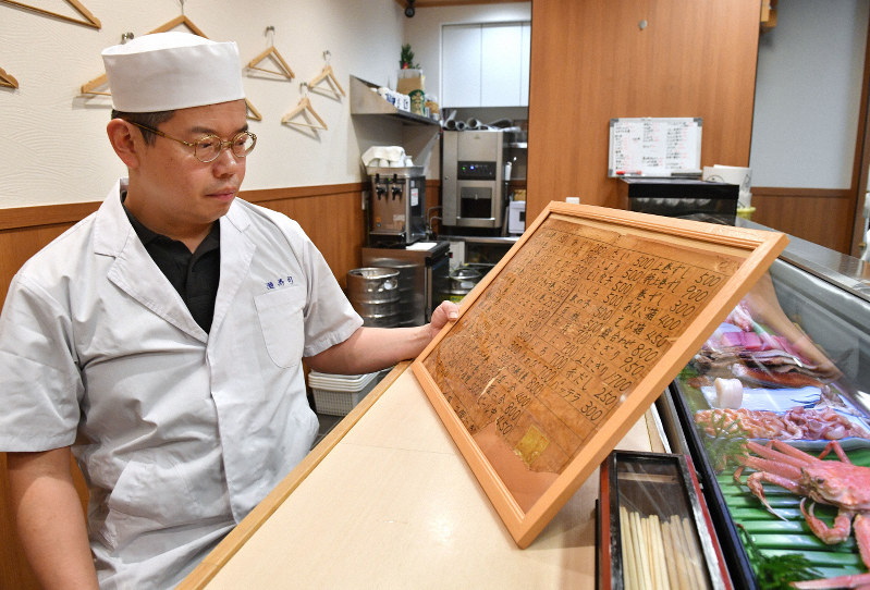 震災で亡くなった母の美智子さんが手書きした値段表を見つめる上野好宏さん=神戸市東灘区で、木葉健二撮影