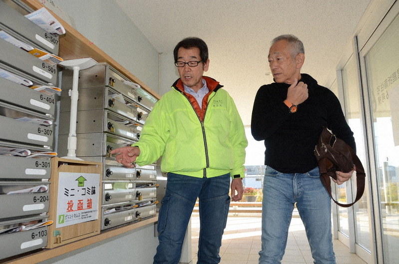 復興住宅の入り口にあるミニコミ誌の投函箱を牧秀一さん(右)に説明する菊田忠衛さん=宮城県気仙沼市で、井上元宏撮影
