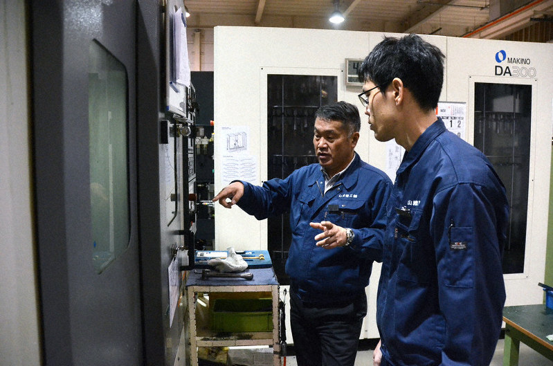 金属を加工する工作機械を前に若手社員を指導する山城機工の岡西栄作社長(左)=神戸市長田区で2019年11月28日、釣田祐喜撮影