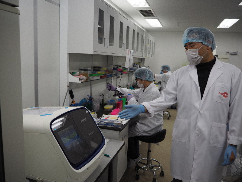 ラボで検体からのDNA抽出などの作業を行うスタッフ。手前は解析機器の説明をするキム・キボム社長=東京都足立区のシーディーエヌエー法医学研究所で2019年11月28日午後5時20分、須田桃子撮影