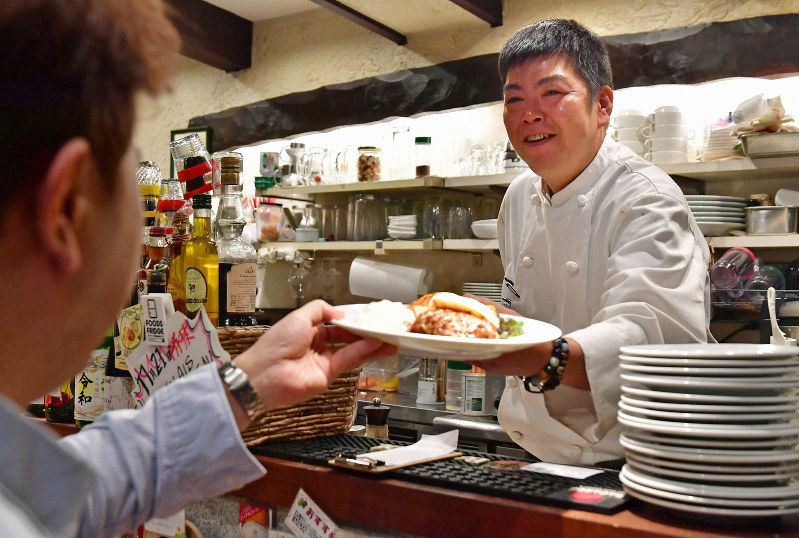 自分の店のカウンター席に座る常連客に料理を出す板倉哲也さん=神戸市東灘区で、小松雄介撮影