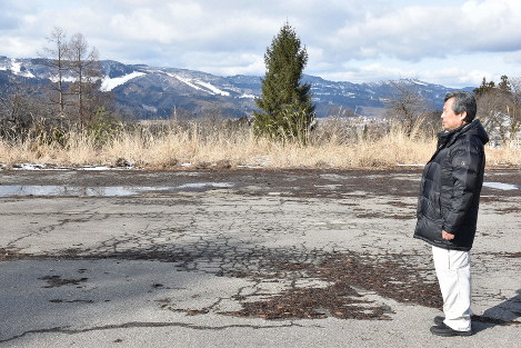 A Minamiuonuma city employee looks at the empty municipal snow storage area, in Minamiuonuma, Niigata Prefecture, on Jan. 17, 2020. There is also very little snow on the mountains in the background. (Mainichi/Aya Iguchi)