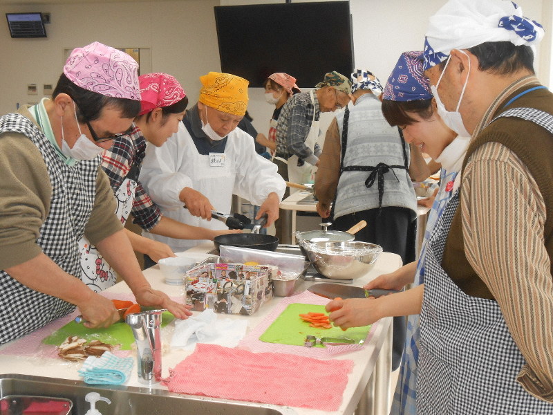 高齢の男性に栄養バランスのよい料理を教える女子学生たち