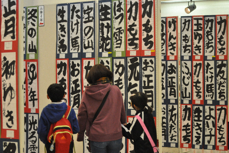 第41回湖西書き初め展に展示された子供たちの作品を眺める親子連れ=高島市安曇川町の藤樹の里文化芸術会館で、塚原和俊撮影