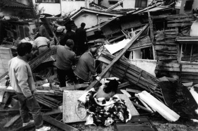 押しつぶされた民家の前で「中に人がいるから早く助けて」と座り込む家人（手前中央）＝兵庫県西宮市松生町で1995年1月17日午前7時撮影