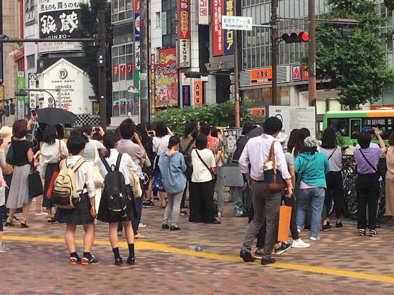 男性アイドルグループのライブ映像を見つめる若者たち=東京・新宿の西武新宿駅前で2018年7月8日撮影