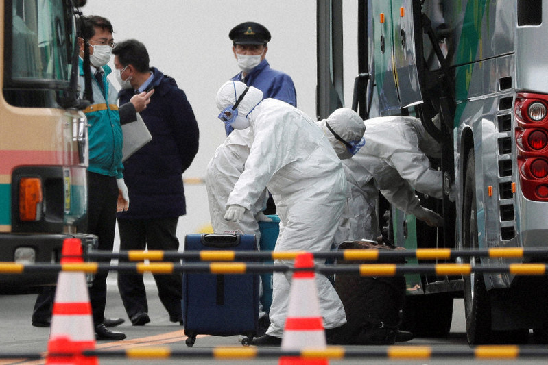 クルーズ船から下船した乗客の荷物をバスに積み込む防護服姿の関係者=横浜港で2020年2月20日、ロイター