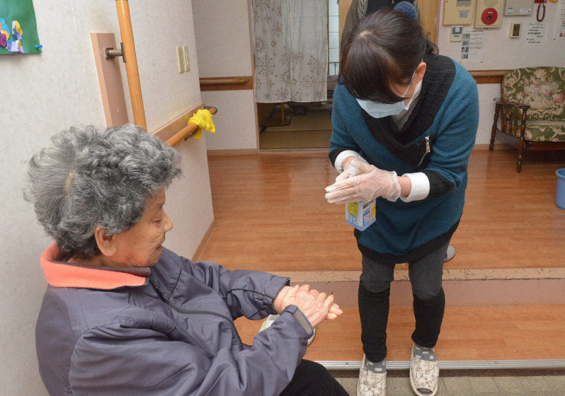 外出先から帰った入居者(左)に、手をアルコール消毒してもらう職員=金沢市浅野本町のグループホーム「おんぼら~と」で2020年2月26日午後4時23分、阿部弘賢撮影