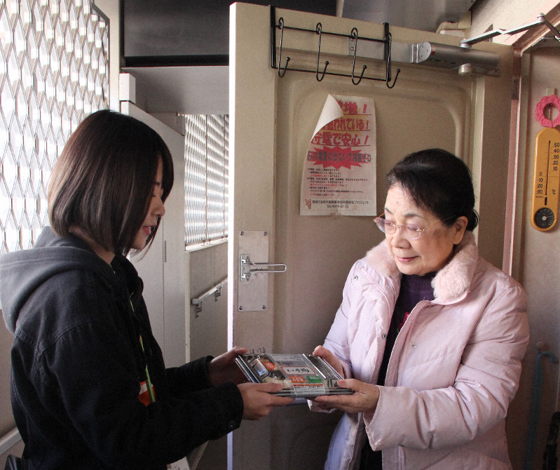 配食サービスのスタッフの斉藤さん(左)から食事を受け取る小池さん=東京都板橋区の高島平団地で2019年12月24日午後1時1分、岡礼子撮影