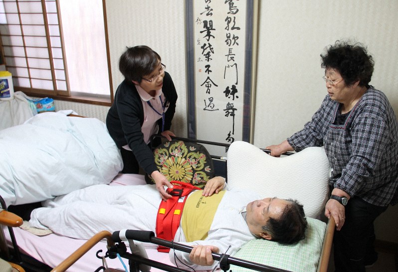 夫を介護する妻(左)とアドバイスをするヘルパー(右)