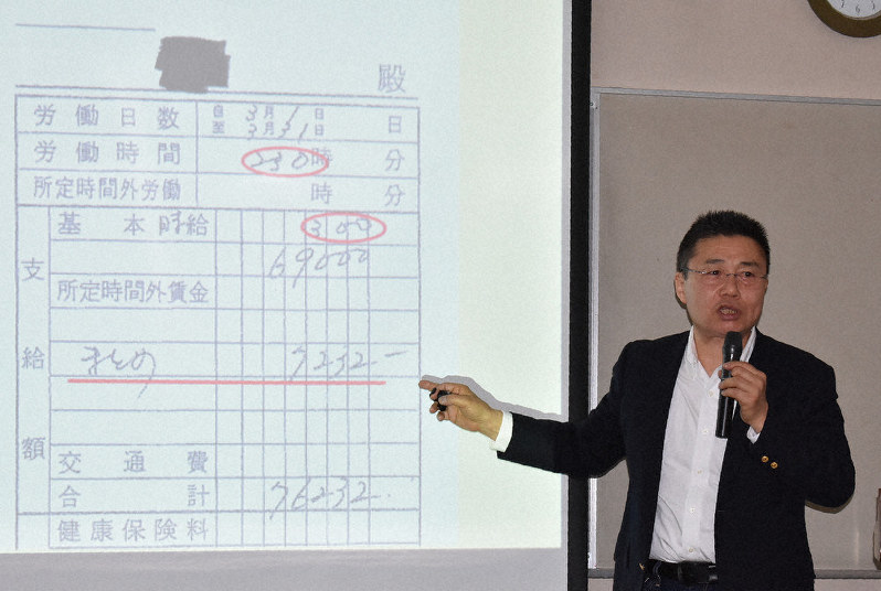 技能実習生が時給300円で働かされていた証拠の給与明細を示す移住連代表の鳥井一平さん=群馬県の伊勢崎市民プラザで