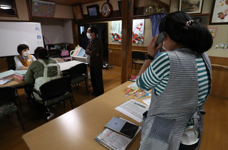 名古屋市から閉鎖要請を受けて利用者への電話連絡に追われるデイサービス施設の関係者(手前)=名古屋市南区で2020年3月6日午後4時22分、兵藤公治撮影
