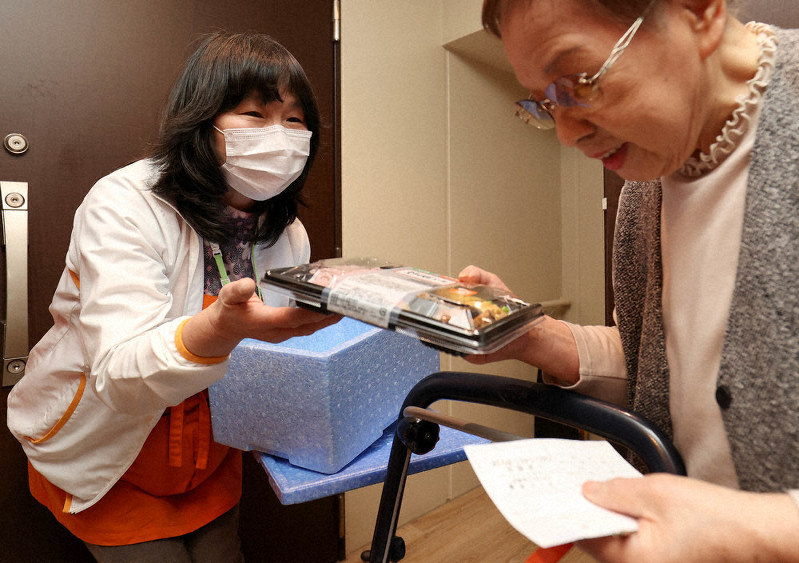 1人暮らしの野口納さん(右)にお弁当を届けるワタミ「まごころスタッフ」の小泉貴世さん=東京都江戸川区で、宮武祐希撮影