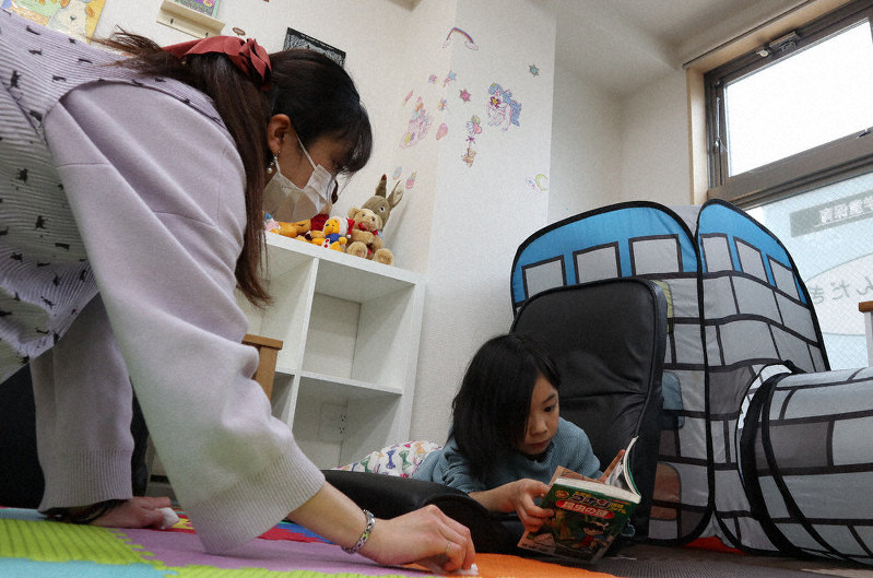 読書をする女児の脇で床を掃除する民間学童施設の女性スタッフ=千脇康平撮影